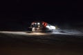 A snow groomer compacting ski runs at night