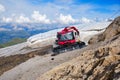 PistenBully snow groomer machine parked next to remaining snow patch, covered with a sun protecting white sheet, at Punta Rocca