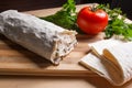 Pita bread or lavash wrapped with cottage cheese or curd, chicken, tomatoes and herbs - dill, onion, parsley on cutting board..