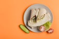 Pita bread roll with chicken, cucumbers, tomatoes and fresh herbs on a flat plate on an orange background