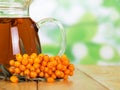 Pitcher drink and bunch sea buckthorn on abstract green background.