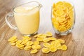 Pitcher with yogurt, scattered cornflakes, glass with corn flakes on wooden table