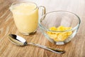 Pitcher with yogurt, transparent bowl with corn flakes, spoon on wooden table Royalty Free Stock Photo