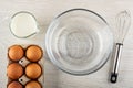 Pitcher with milk, box with brown eggs, bowl, whisk on wooden table. Top view Royalty Free Stock Photo