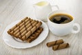 Pitcher with milk, brown wafer rolls with filling in plate, black coffee in cup, halves of wafer roll on table Royalty Free Stock Photo