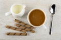 Pitcher with milk, wafer rolls with chocolate filling, coffee with milk in cup, spoon on table. Top view Royalty Free Stock Photo