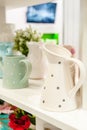 A pitcher and a set of clean dishes and home furnishings on white shelves in the kitchen