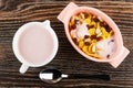 Pitcher with yogurt, pink bowl with corn flakes, raisin, peanut and yogurt, spoon on wooden table. Top view