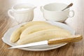 Pitcher with yogurt, spoon in bowl, peeled bananas, knife in dish on wooden table