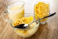 Pitcher with yogurt, spoon in bowl with corn flakes and fruit yogurt, glass with cornflakes on wooden table Royalty Free Stock Photo