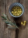 Pitted olives in a bowl with leaves on wood background