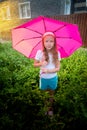 Pity blonde child with pink umbrella under the summer rain with su. Girl enjoying rainfall. Kid playing on the nature Royalty Free Stock Photo