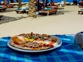 Pizza with bacon and green spicy pepper on a plate on a blue tablecloth in a cafe.