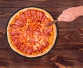 Pizza bacon on slate bottom, on wooden table, hand cutting pizza