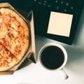 Pizza in box, cup of coffee, laptop and empty sticker on table in office. Royalty Free Stock Photo