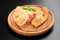 Pizza calzone with basil leaves close up on wooden round board cutted with tomato cheese and ham