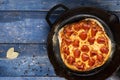 Pizza in a cast iron skillet on a blue wooden surface