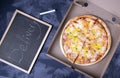 Pizza with cheese in a cardboard box and the chalkboard with the word delivery written on it