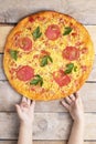 Margarita pizza with cheese and tomatoes on wooden table, kids hands hold pizza,top view and place for text