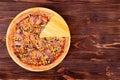 Pizza with chicken breast, corn, bacon and mushrooms, without one slice on a wood plate which is on wooden rustic table Royalty Free Stock Photo