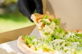 Pizza close-up in hands in medical gloves. Courier in medical mask holds pizza in hands and looks to pizza with green