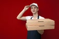 Pizza delivery man in uniform on a red background gives boxes of food, the courier guy gives the finished order Royalty Free Stock Photo
