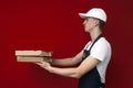 Pizza delivery man in uniform on a red background gives boxes of food, the courier guy gives the finished order Royalty Free Stock Photo