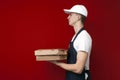 Pizza delivery man in uniform on a red background gives boxes of food, the courier guy gives the finished order Royalty Free Stock Photo