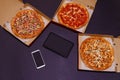 Pizza delivery. Opened boxes with pizza, tablet and smartphone with blank screen. Top view, copy space