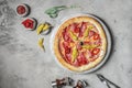 pizza with ham, mozzarella, marinated peppers on marble round tray. Garnished on grey stone backdrop with pizza ingredients