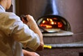 Pizza maker in pizzeria makes pizza in wood-fired oven.