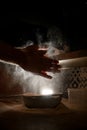 Pizza maker's hands sift flour on a sieve before preparing pizza in the dark kitchen