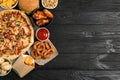 Pizza, onion rings and other fast food on black wooden table, flat lay with space for text Royalty Free Stock Photo