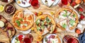 Pizza party table. Top view glasses with red wine and dinner plates on rustic wooden table with hot pizzas, italian appetizers,