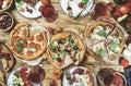 Pizza party table. Top view glasses with red wine, rustic wooden table with hot pizzas, italian appetizers, salads, cheese, fruits