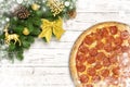 Pizza pepperoni Christmas snowflake with fir branches and new year toy ball, deer or reindeer, bow on white wood board Royalty Free Stock Photo