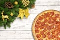 Pizza pepperoni Christmas snowflake with fir branches and new year toy ball, deer or reindeer, pine cone, on white wood board Royalty Free Stock Photo
