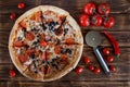 Pizza with pepperoni, salami, mushrooms and olives lies on a rustic table alongside red pepper, tomatoes and a special circular Royalty Free Stock Photo