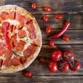 Pizza with pepperoni, salami and red chilli pepper lies on a plank table next to a bunch of tomatoes. Square Royalty Free Stock Photo