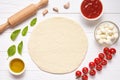Pizza preparation. Baking ingredients on the kitchen table: rolled dough, mozzarella, tomatoes sauce, basil, olive oil