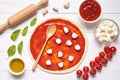 Pizza preparation. Ingredients on the kitchen table: rolled dough with tomatoes sauce, basil, olive oil, mozzarella Royalty Free Stock Photo