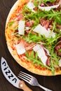 Pizza with prosciutto (parma ham), arugula (salad rocket) and parmesan on dark wooden background top view