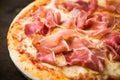 Pizza with prosciutto (parma ham) on dark wooden background close up