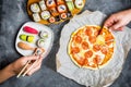 Pizza with salami, set of sushi rolls and hands take food. Food background. Flat lay, top view.