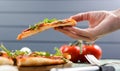 Pizza slice in hand. Thin pizza with fresh arugula, tomatoes and