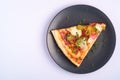 Pizza slice with pepperoni, salami, melted mozzarella cheese, pickles and dill in black plate on white background Royalty Free Stock Photo