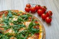 Pizza with tomato sauce, shrimp, garlic, arugula and cheese detail with cherry tomatoes in background on wooden board