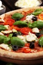 Pizza with tomatoes, mozzarella cheese, black olives and basil. Delicious italian pizza on wooden pizza board Royalty Free Stock Photo