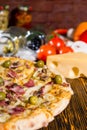 Pizza on wooden table, tomatoes, cheese and other vegetables in