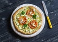 Pizza with zucchini, tomatoes, onions and feta cheese on a light board on dark wooden background.